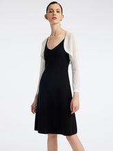 A woman is wearing a white cardigan and a sheath black dress.
